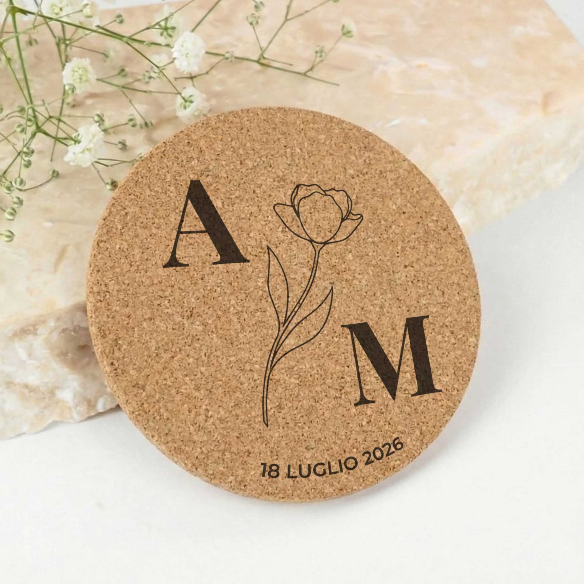 Sottobicchiere segnaposto matrimonio personalizzato in sughero tondo tenuto tra le mani su tavola apparecchiata elegante con fiori bianchi.